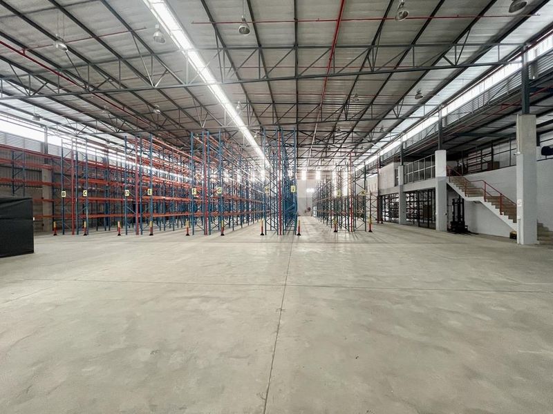 Spacious industrial warehouse featuring high ceilings, extensive steel racking systems, polished concrete flooring, and a mezzanine level with integrated staircase access.