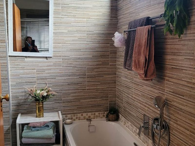 A bathroom featuring full-height textured wall tiling, a standard bathtub with a handheld shower mixer, and a wall-mounted towel rail.