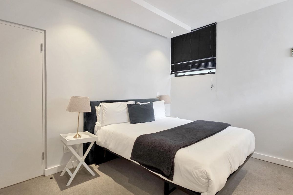 A well-maintained bedroom featuring neutral carpet flooring, a modern drop ceiling bulkhead with recessed lighting, and fitted venetian blinds.