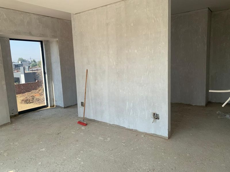 An unfinished interior space featuring plastered walls, concrete flooring, and a large window, currently in a shell condition awaiting final finishes.