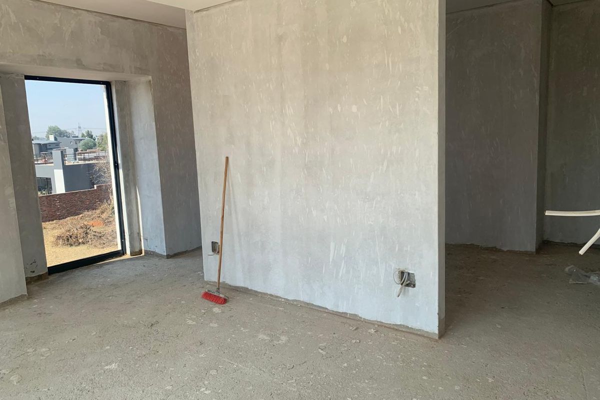 An unfinished interior space featuring plastered walls, concrete flooring, and a large window, currently in a shell condition awaiting final finishes.