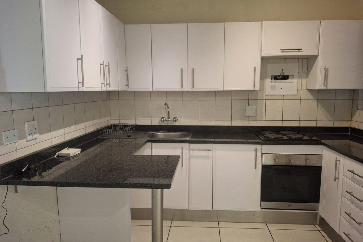 A functional kitchen featuring white cabinetry, dark granite countertops, a built-in oven, electric hob, and tiled finishes throughout.