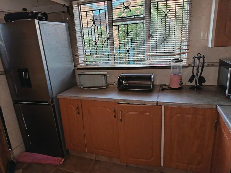 A functional kitchen area featuring wood-look laminate cabinetry, tiled flooring, and security bars on the window.