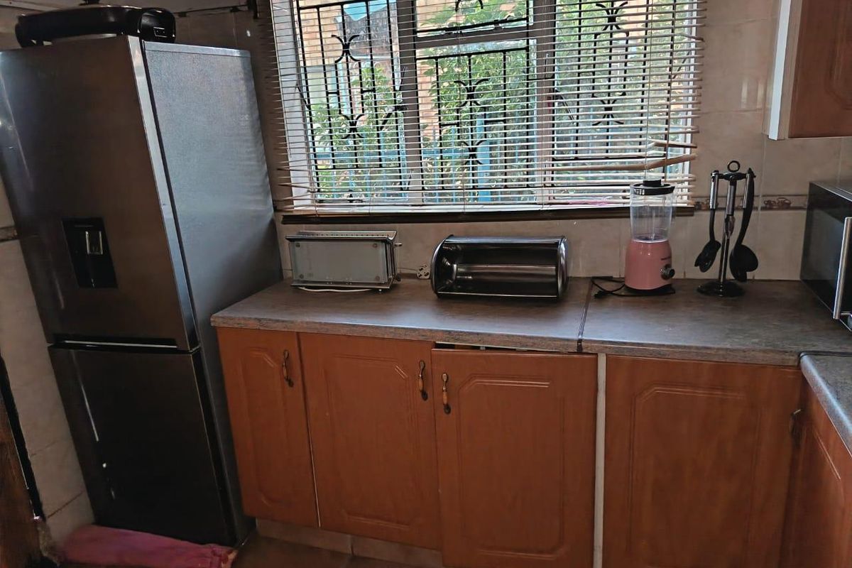 A functional kitchen area featuring wood-look laminate cabinetry, tiled flooring, and security bars on the window.