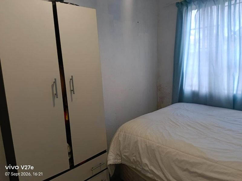 A bedroom featuring a built-in wardrobe, showing visible signs of wall dampness and paint deterioration requiring maintenance.