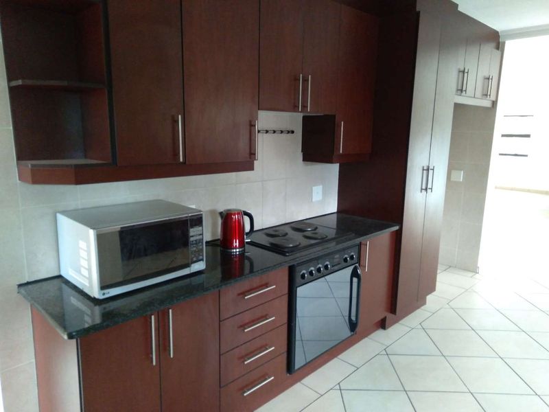 A functional kitchen featuring dark wood cabinetry, granite countertops, built-in oven, electric hob, and tiled flooring.