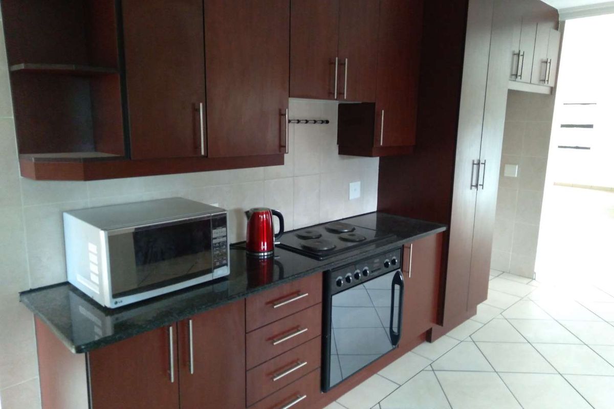 A functional kitchen featuring dark wood cabinetry, granite countertops, built-in oven, electric hob, and tiled flooring.