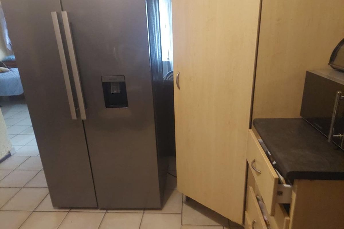 A kitchen area featuring light wood-finish cabinetry, dark laminate countertops, and tiled flooring, showing signs of standard wear and tear.