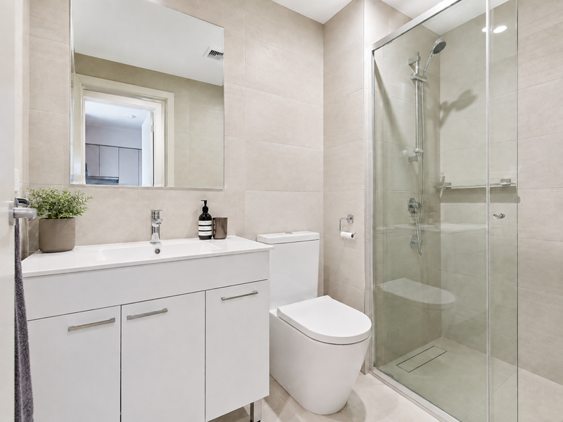 Modern bathroom featuring a sleek vanity, dual-flush toilet, and a glass-enclosed shower with neutral floor-to-ceiling tiling.
