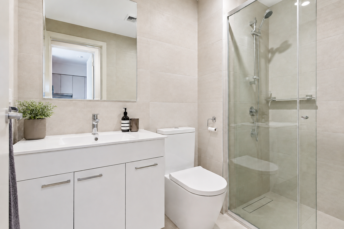 Modern bathroom featuring a sleek vanity, dual-flush toilet, and a glass-enclosed shower with neutral floor-to-ceiling tiling.
