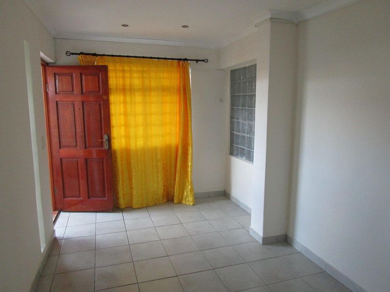 An empty living area featuring neutral tiled flooring, a glass block feature window, and a solid timber entrance door.