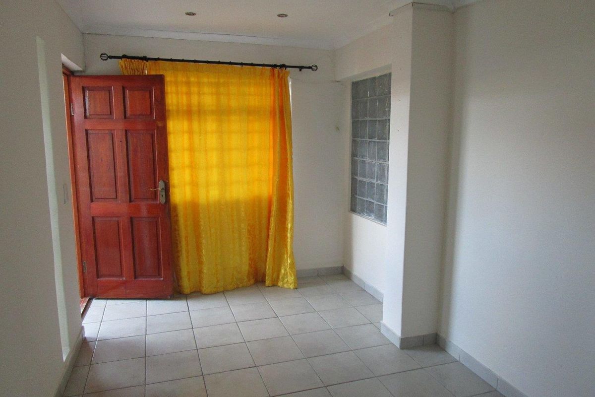 An empty living area featuring neutral tiled flooring, a glass block feature window, and a solid timber entrance door.