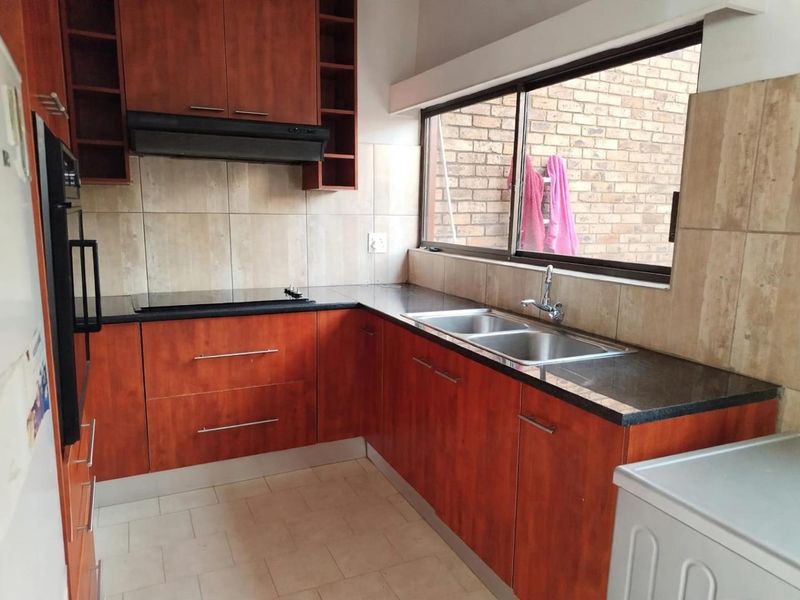 A functional kitchen featuring cherry-wood cabinetry, granite countertops, a double stainless steel sink, and built-in cooking appliances with a tiled backsplash.