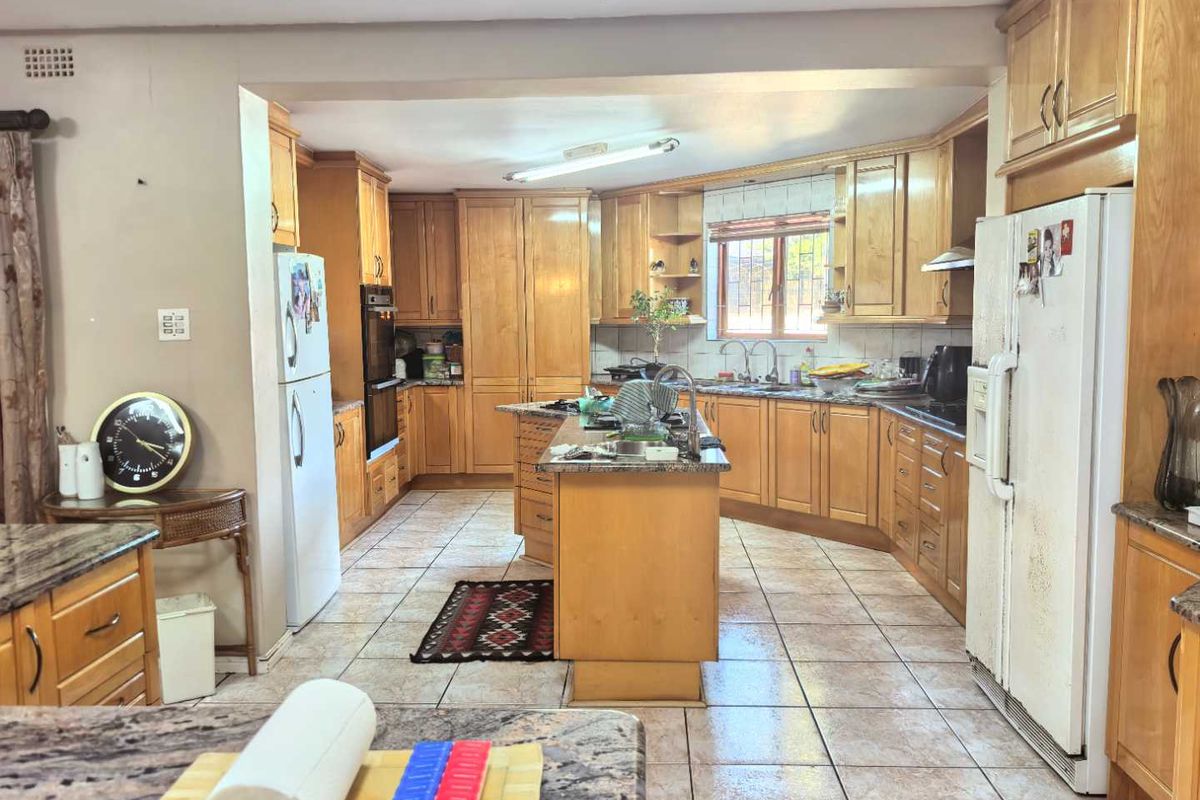 Spacious kitchen featuring extensive wooden cabinetry, a central island with granite countertops, and tiled flooring, offering ample storage and workspace.