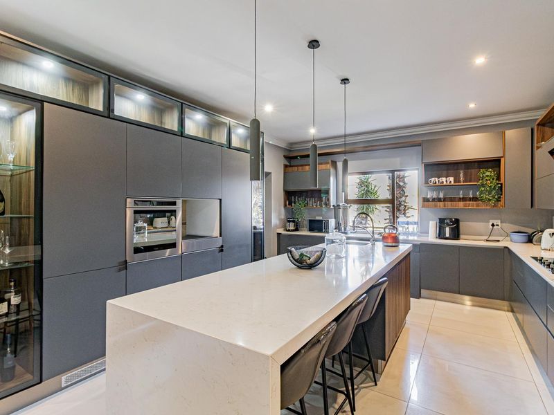 Modern, high-end kitchen featuring sleek dark cabinetry, a large quartz island, integrated appliances, and elegant pendant lighting.