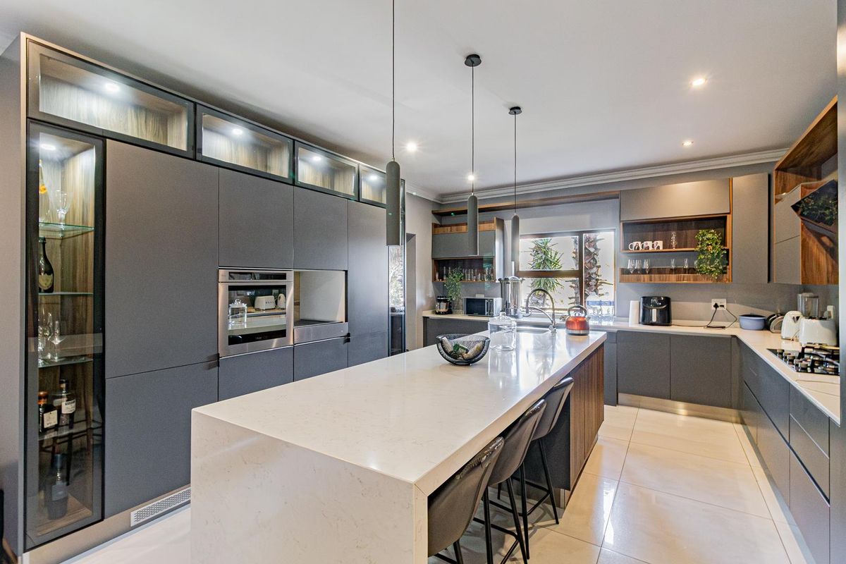 Modern, high-end kitchen featuring sleek dark cabinetry, a large quartz island, integrated appliances, and elegant pendant lighting.