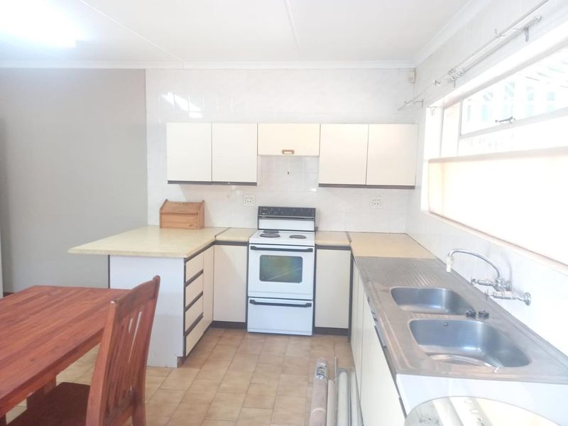A functional kitchen featuring white cabinetry, laminate countertops, a freestanding stove, and a double stainless steel sink with tiled splashbacks.