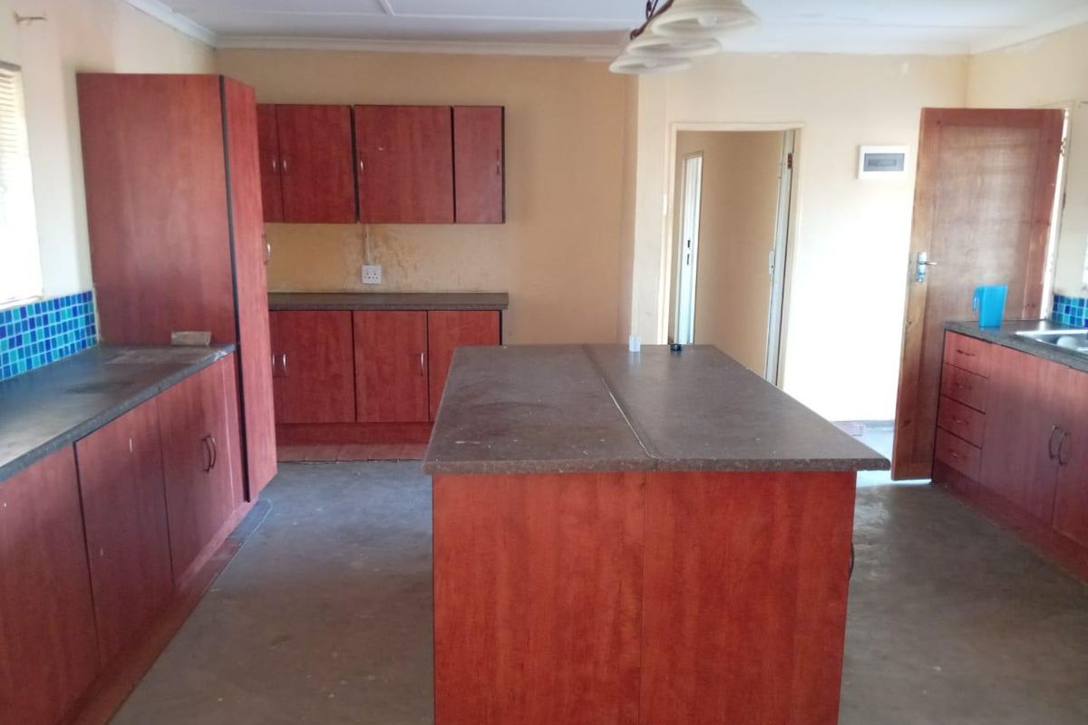 A dated kitchen featuring wooden cabinetry, a central island, and tiled splashbacks, offering a functional layout in need of cosmetic updates.