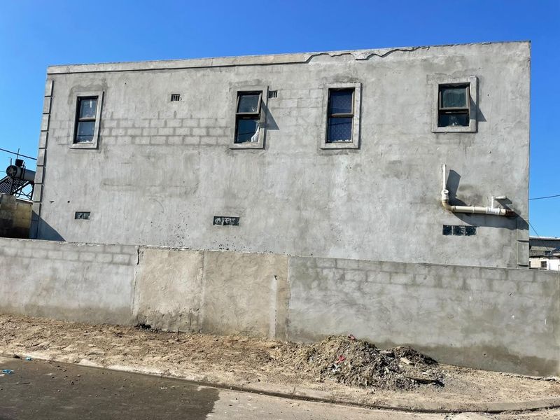 Exterior view of a building facade featuring unfinished cement plaster, exposed plumbing, and multiple casement windows.