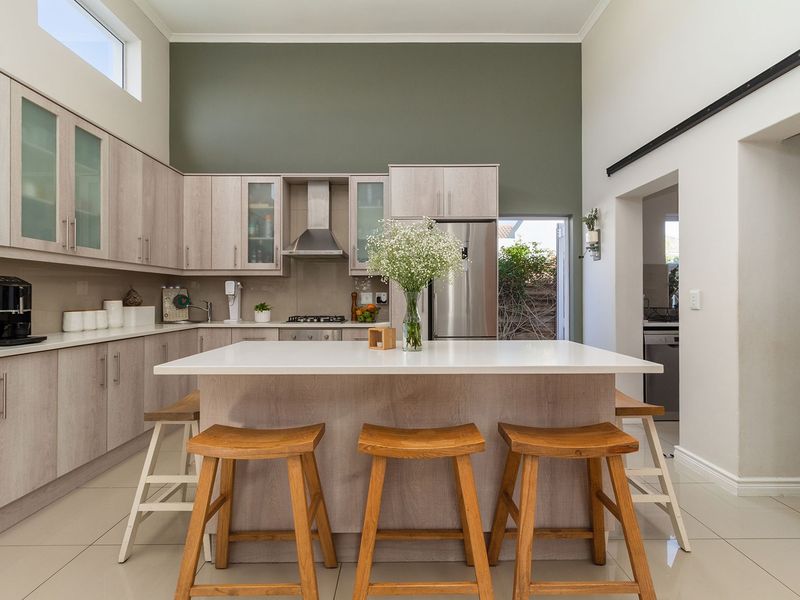 Modern kitchen featuring light wood cabinetry, stone countertops, a central island, and high ceilings with an integrated gas hob and extractor fan.