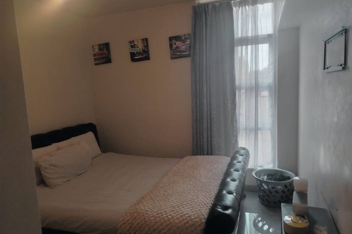A compact bedroom featuring tiled flooring and a large window with curtains, providing natural light to the space.