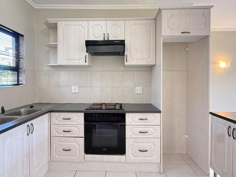 A functional kitchen featuring light-toned cabinetry, a built-in oven and hob, tiled backsplash, and a dedicated space for a refrigerator.