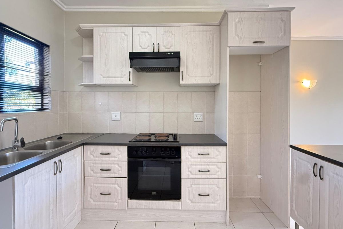 A functional kitchen featuring light-toned cabinetry, a built-in oven and hob, tiled backsplash, and a dedicated space for a refrigerator.