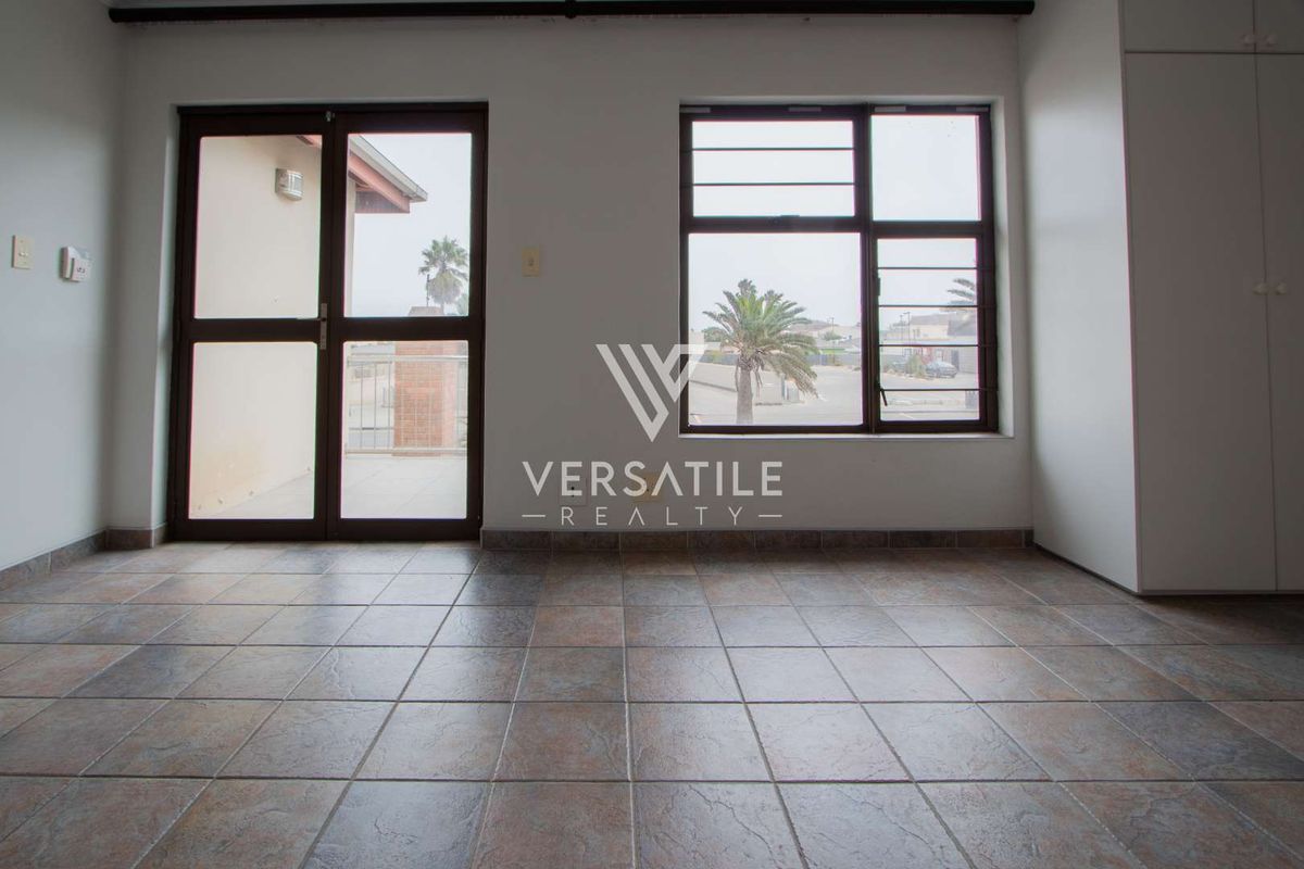 An empty living area featuring tiled flooring, built-in cabinetry, and large windows providing natural light and access to an outdoor patio space.