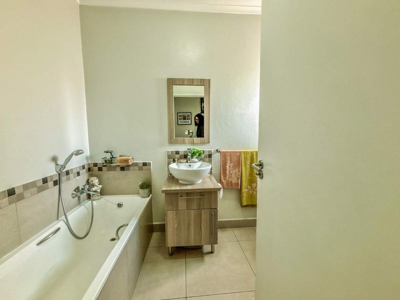 A functional bathroom featuring a built-in bathtub with a handheld shower mixer, a modern vessel sink vanity, and neutral wall tiling.