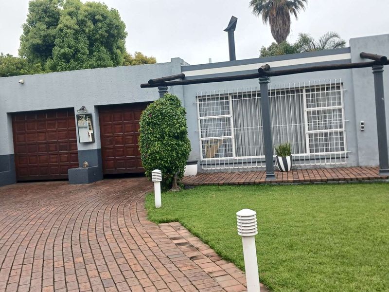 Front view of the property featuring a brick paved driveway, double wooden garage doors, a small lawn, and a covered patio area with security bars.