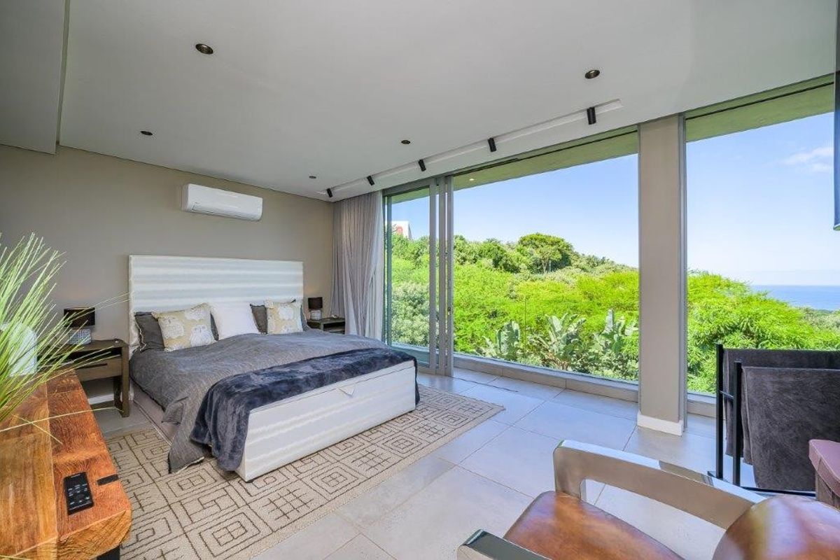 Spacious bedroom featuring floor-to-ceiling sliding glass doors that open to a lush green view, complemented by modern tiled flooring and recessed lighting.