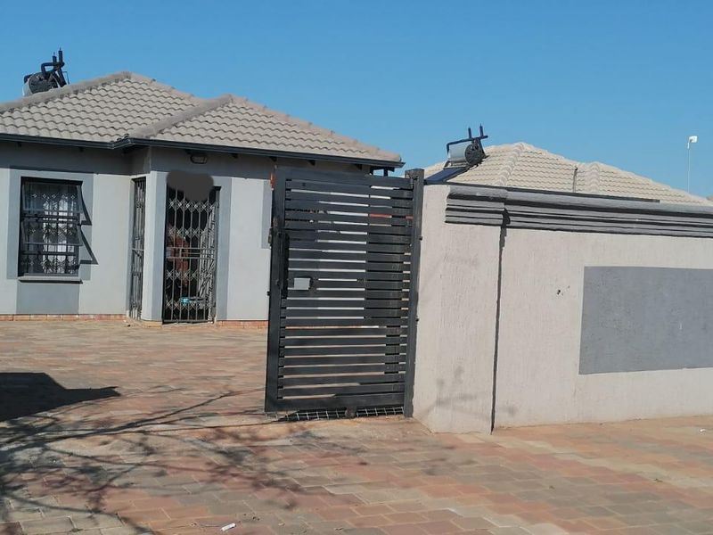 Front view of a single-story house featuring a paved driveway, secure gated entrance, and solar geyser installation on the tiled roof.