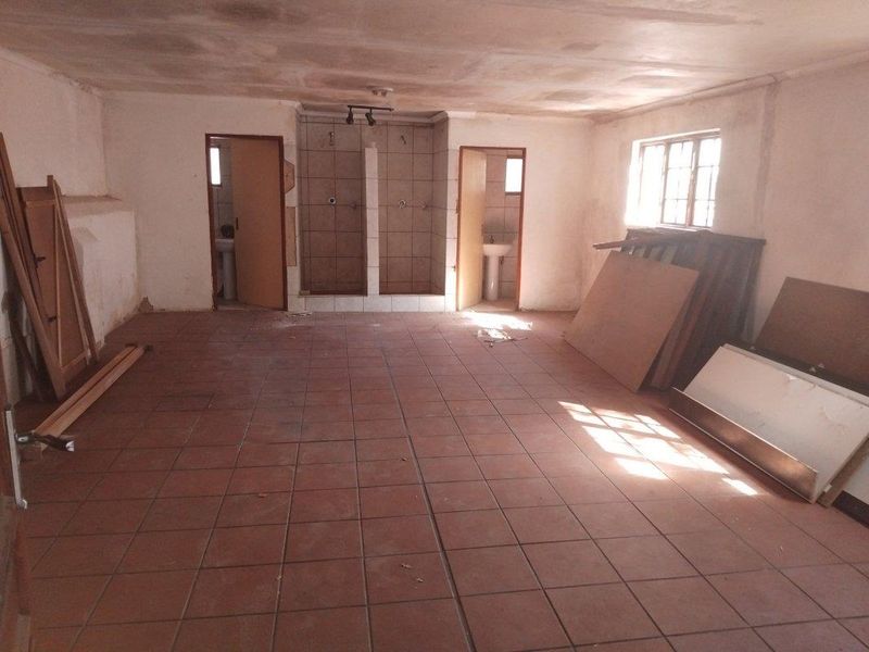 A large, vacant utility space featuring tiled flooring, dual shower stalls, and two separate wash basin areas, requiring significant renovation and cosmetic updates.