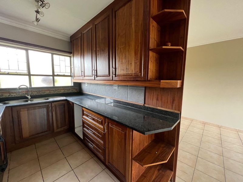 A functional kitchen featuring dark wood cabinetry, granite countertops, and a double basin sink, with tiled flooring and neutral wall finishes.