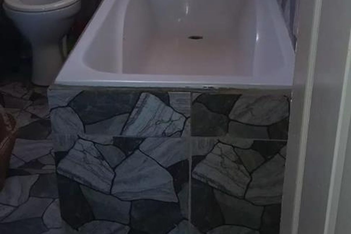 A compact bathroom featuring a bathtub and toilet with distinctive stone-patterned wall and floor tiling.