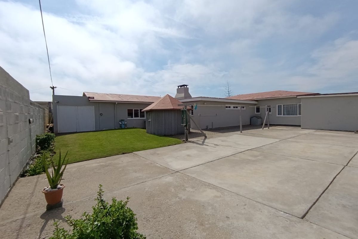 Spacious rear exterior area featuring a large concrete patio, a well-maintained lawn, and a detached circular structure with a tiled roof.