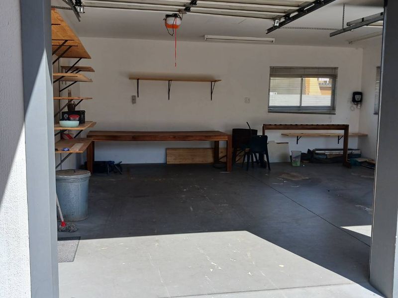 Spacious garage featuring concrete flooring, built-in workbench, and wall-mounted shelving, providing ample storage and workspace potential.