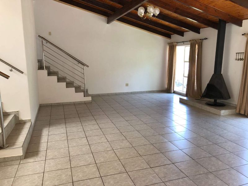 Spacious living area featuring tiled floors, exposed timber ceiling beams, a modern stainless steel staircase, and a prominent freestanding fireplace.