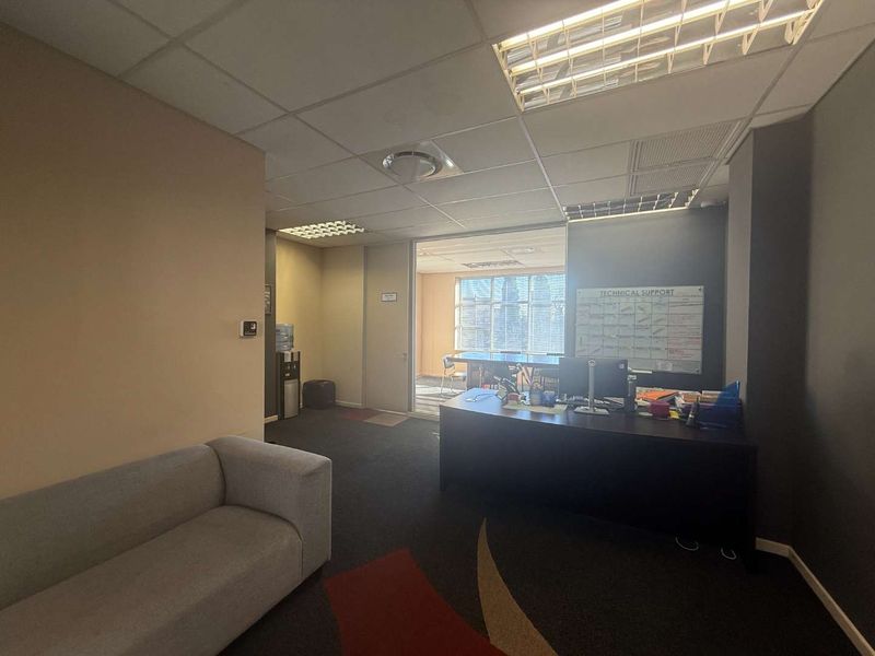 A functional office space featuring a suspended ceiling, recessed lighting, and a glass partition leading to an adjacent workspace.