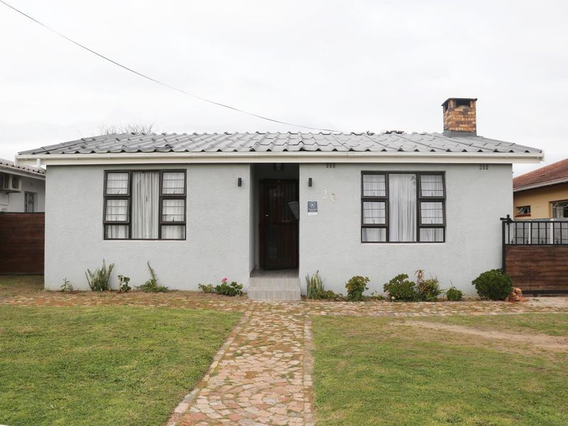 Front elevation of a single-story house featuring a metal roof, brick chimney, and paved walkway leading to the entrance.