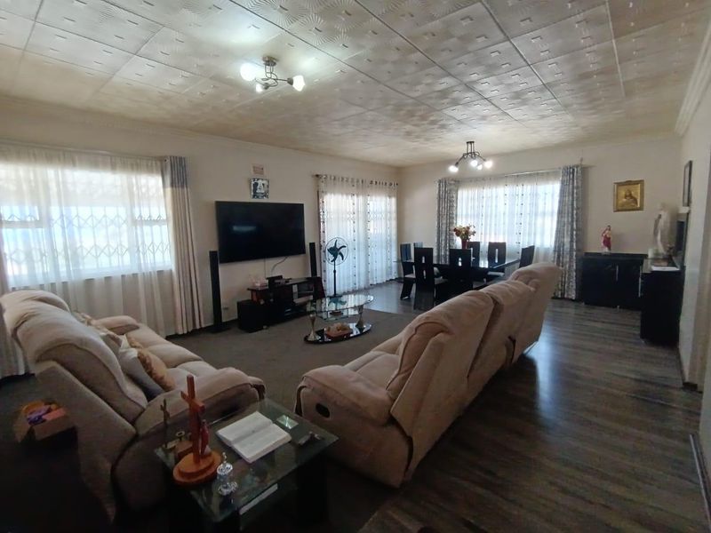 Spacious open-plan living and dining area featuring laminate flooring, textured ceiling tiles, and large windows with security bars.