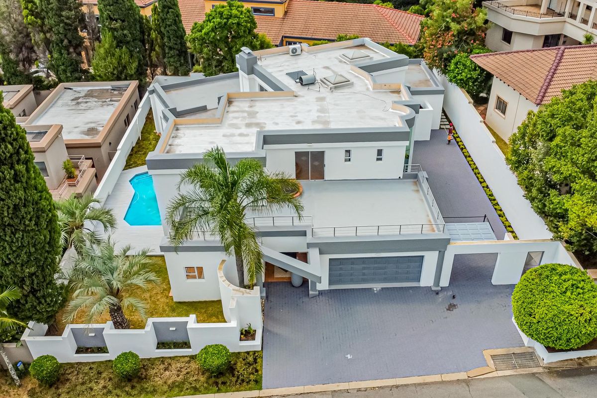 Aerial view of a modern multi-level house featuring a swimming pool, paved driveway, garage, and flat roof design with balcony access.