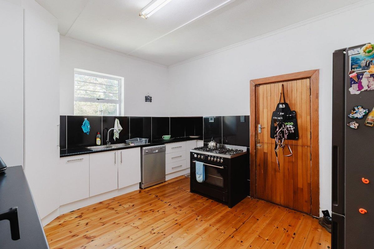 Functional kitchen featuring timber flooring, white cabinetry, black tiled splashback, and a freestanding gas stove with oven.