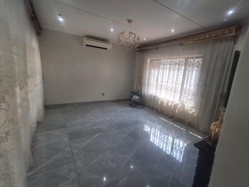Spacious living room featuring large-format grey porcelain floor tiles, recessed downlighting, and a wall-mounted air conditioning unit.