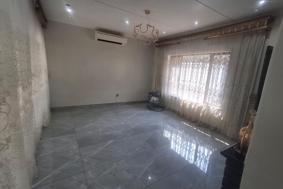 Spacious living room featuring large-format grey porcelain floor tiles, recessed downlighting, and a wall-mounted air conditioning unit.