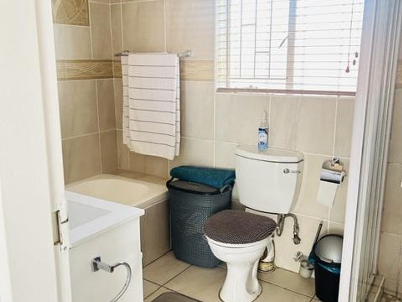 A functional bathroom featuring a built-in bathtub, separate shower enclosure, vanity cabinet, and neutral ceramic tiling throughout.