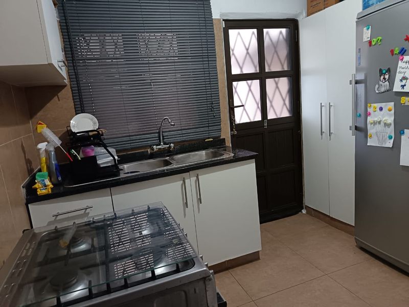 A functional kitchen featuring granite countertops, a double bowl sink, built-in cabinetry, a gas hob, and direct access to the exterior via a security door.