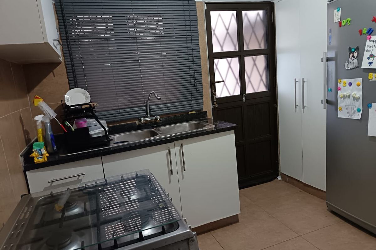 A functional kitchen featuring granite countertops, a double bowl sink, built-in cabinetry, a gas hob, and direct access to the exterior via a security door.