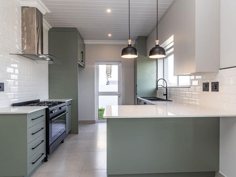 Modern kitchen featuring sage green cabinetry, white quartz countertops, subway tile backsplash, gas stove, and contemporary pendant lighting.