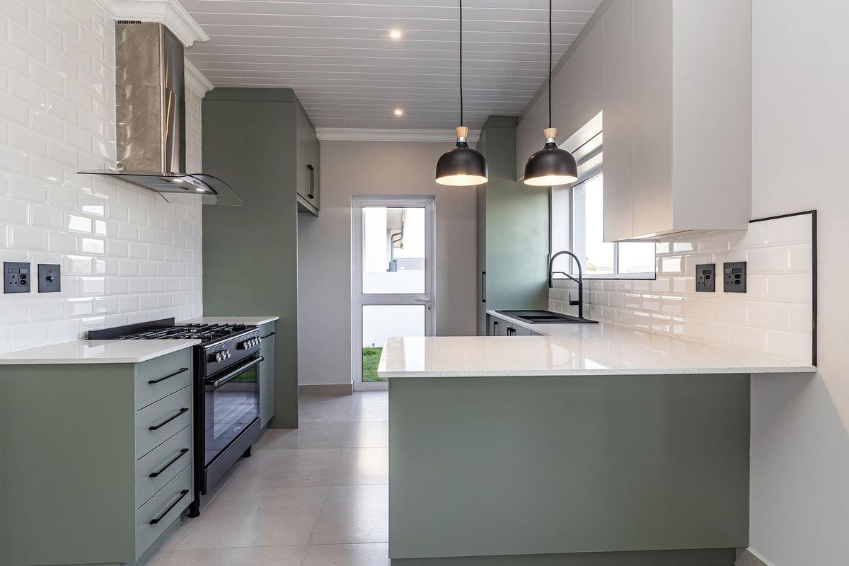 Modern kitchen featuring sage green cabinetry, white quartz countertops, subway tile backsplash, gas stove, and contemporary pendant lighting.